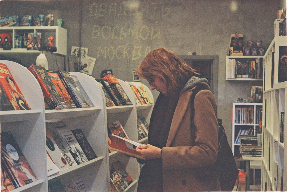 A woman enjoys reading in a cozy bookstore in Moscow, Russia, surrounded by shelves of books.